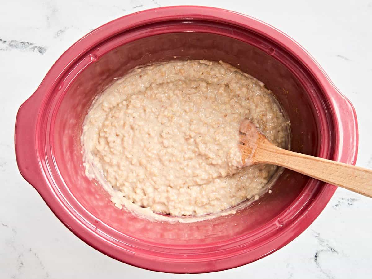 A wooden spoon mixing slow cooker steel cut oats in a crockpot.