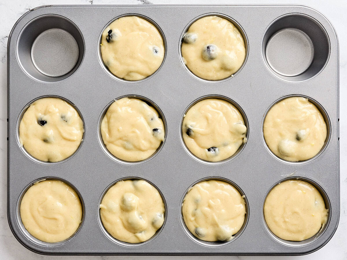 Blueberry lemon muffin batter divided into individual muffin wells in a muffin pan.