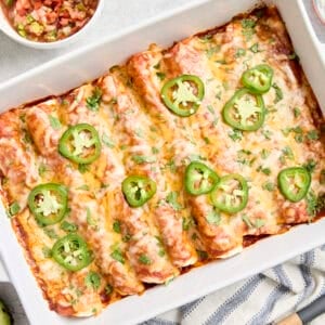 Overhead view of chicken enchiladas in a baking dish topped with fresh cilantro and sliced jalapenos.