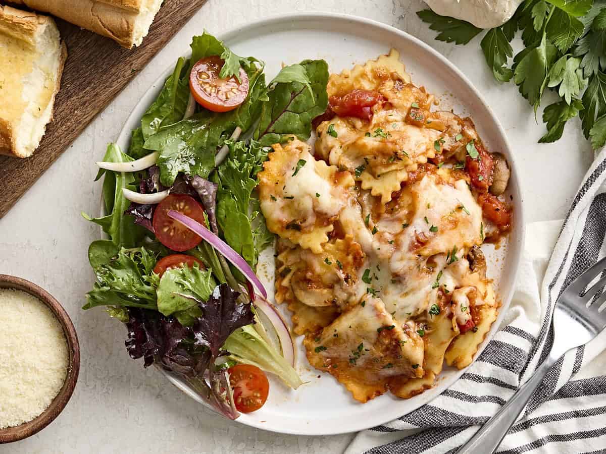 Overhead view of cheesy ravioli on a plate with a side salad.
