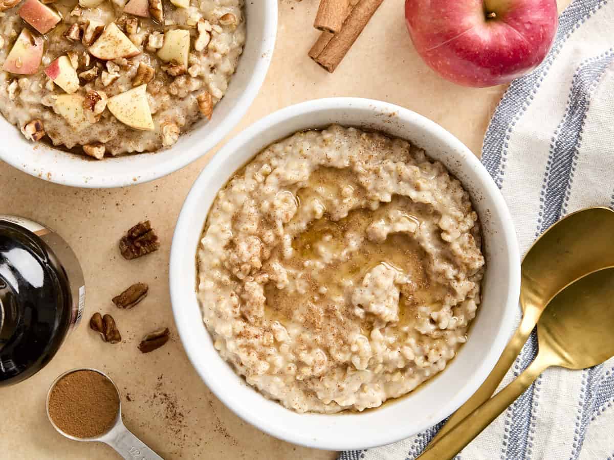 Overhead view of crockpot steel cut oatmeal in bowls, one bowl is topped with maple syrup and cinnamon and the other is topped with chopped apples and walnuts.