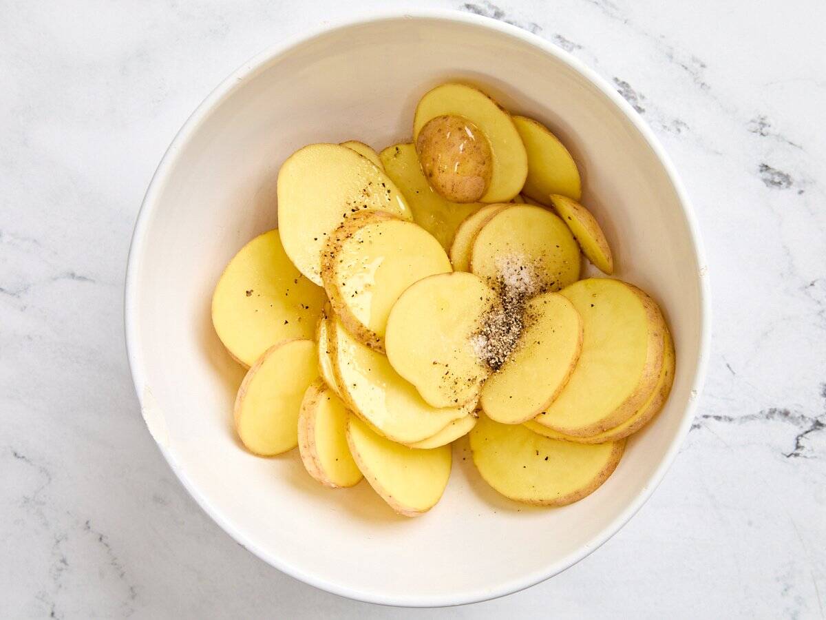Sliced yukon gold potatoes in a bowl with seasonings.