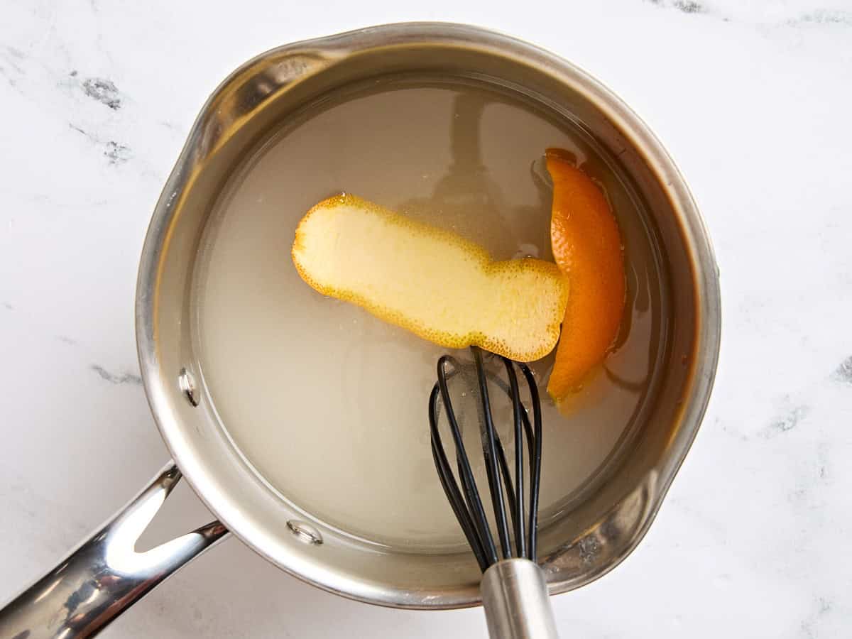 A whisk in a pot with simple syrup and orange peel.