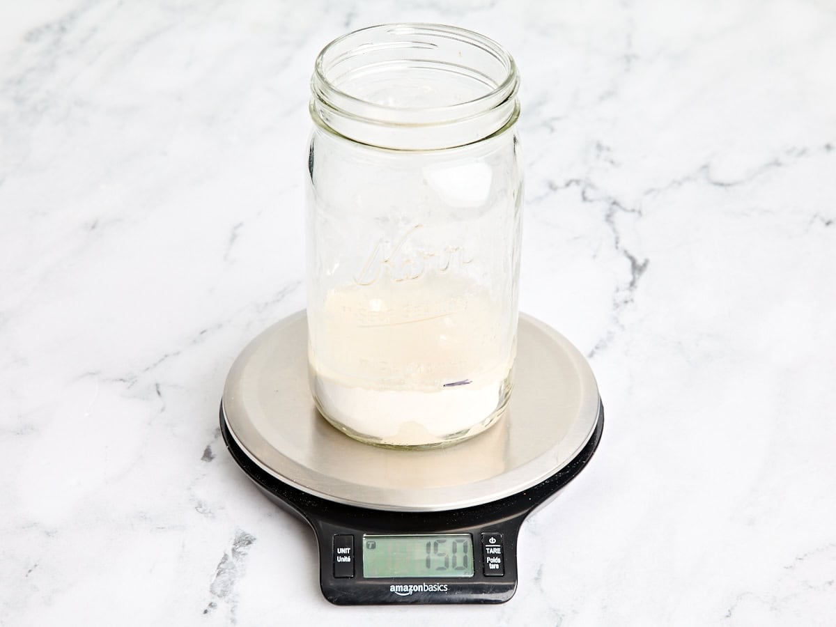 Water added to flour in an empty mason jar on kitchen scales.