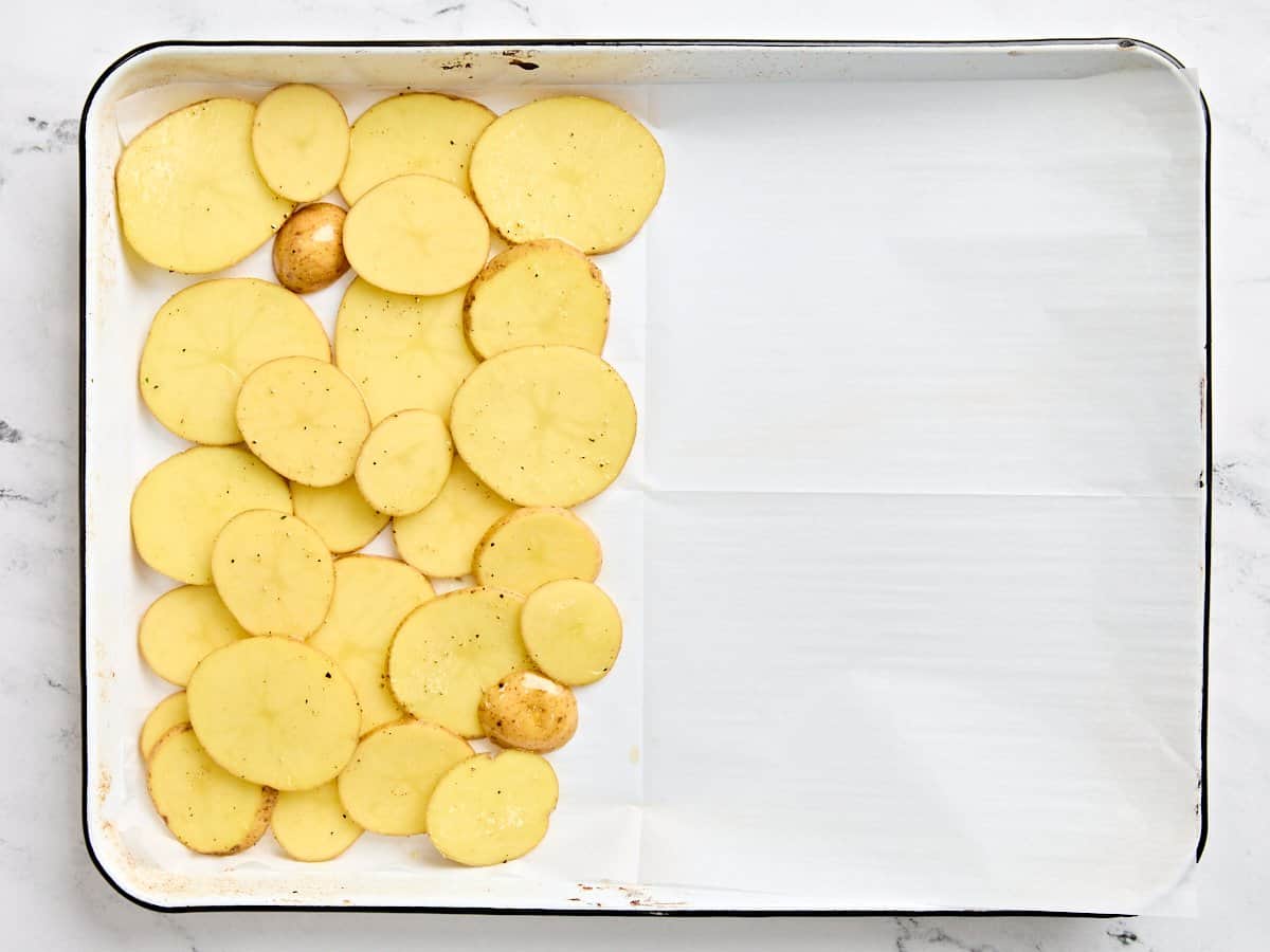 Sliced and seasoned yukon gold potatoes on a sheet pan.