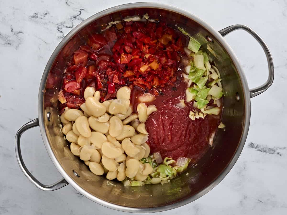 Canned tomatoes, roasted red peppers, and butter beans in a soup pot with diced cabbage and onion.