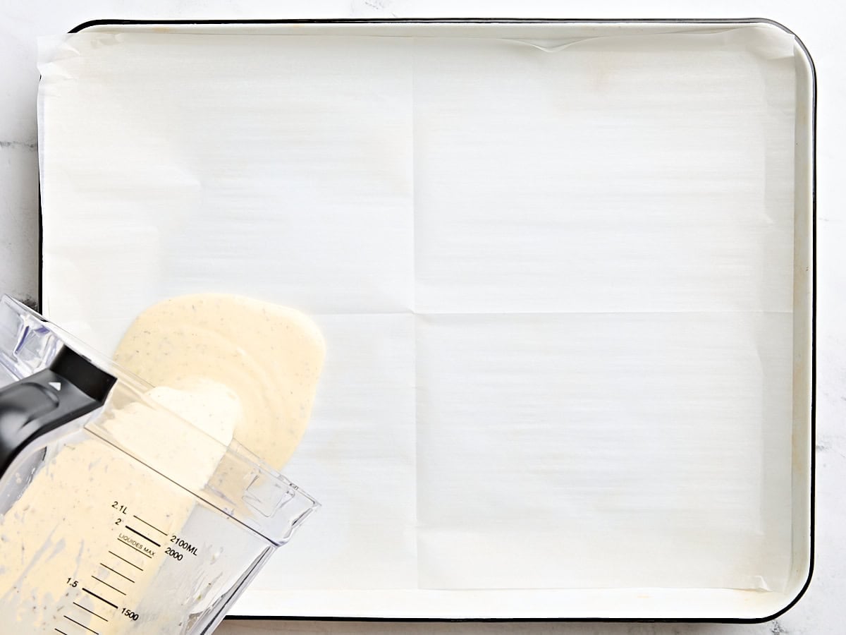 Cottage cheese wrap mixture being poured onto a parchment lined baking sheet.