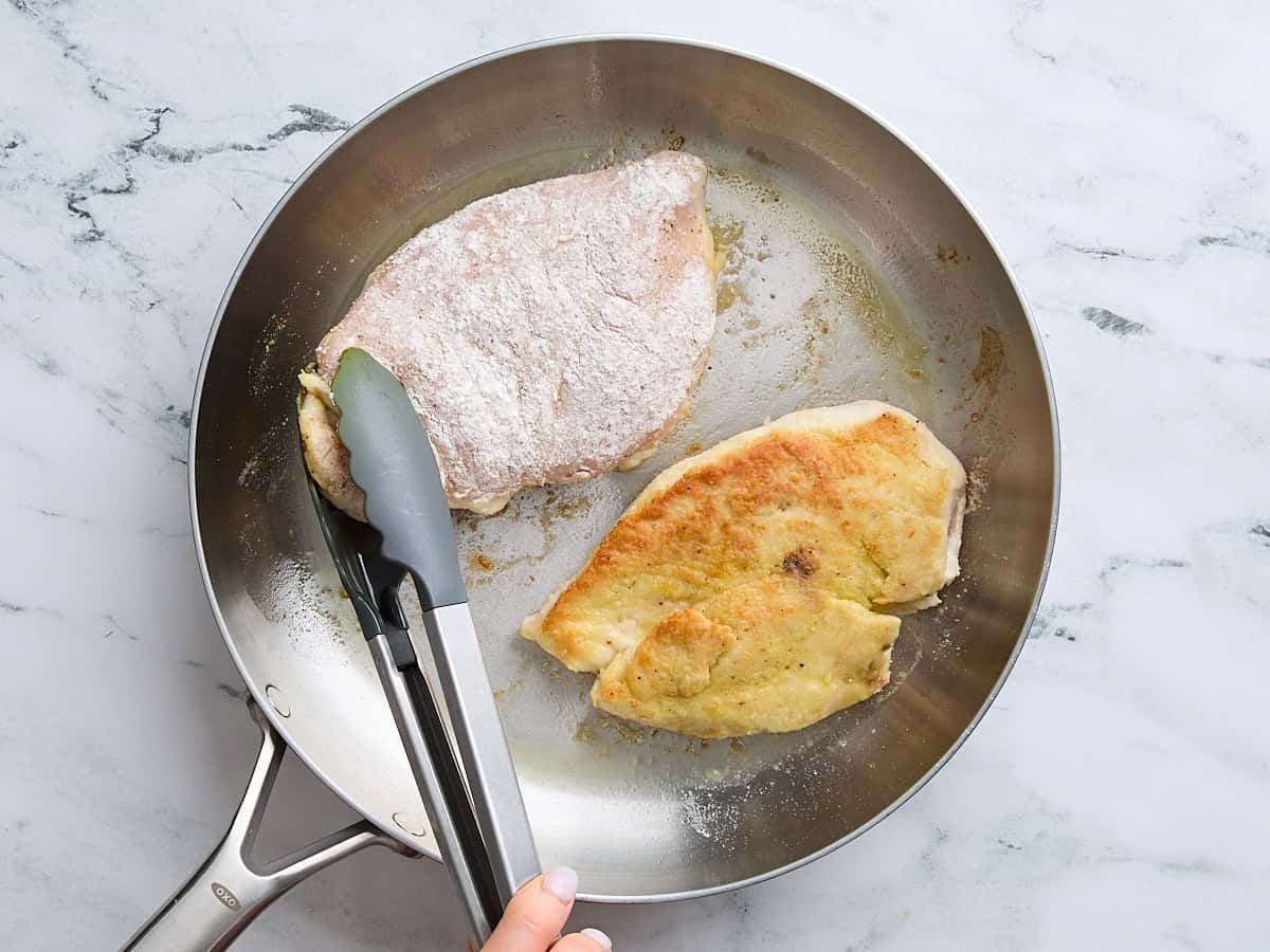 Flour coated chicken breasts cooking a in a skillet.