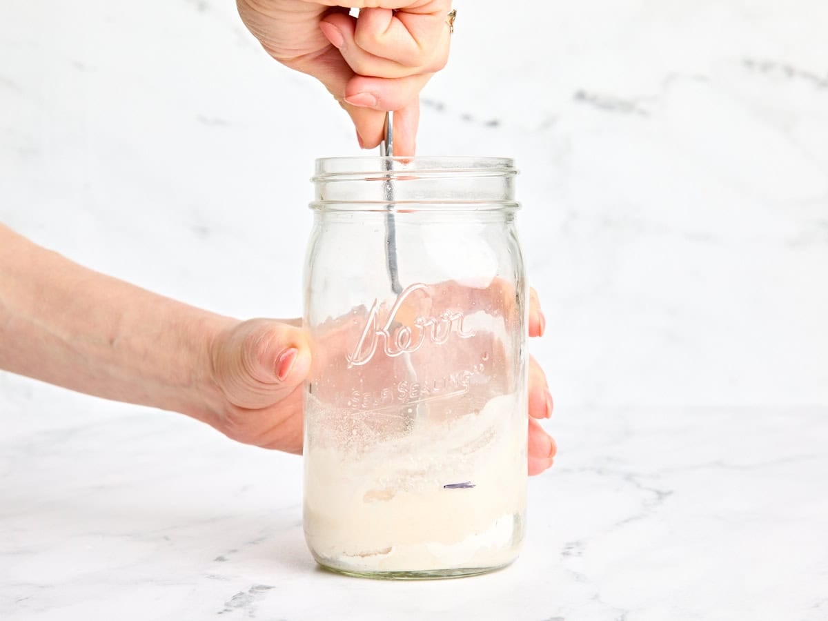 Flour and water being mixed together with a spoon in a mason jar to make a sourdough starter.