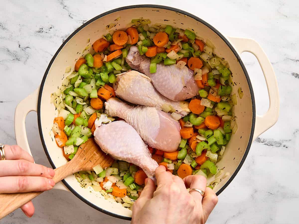 Chicken drumsticks added to a stock pot of sauteed carrots, celery, and onion.