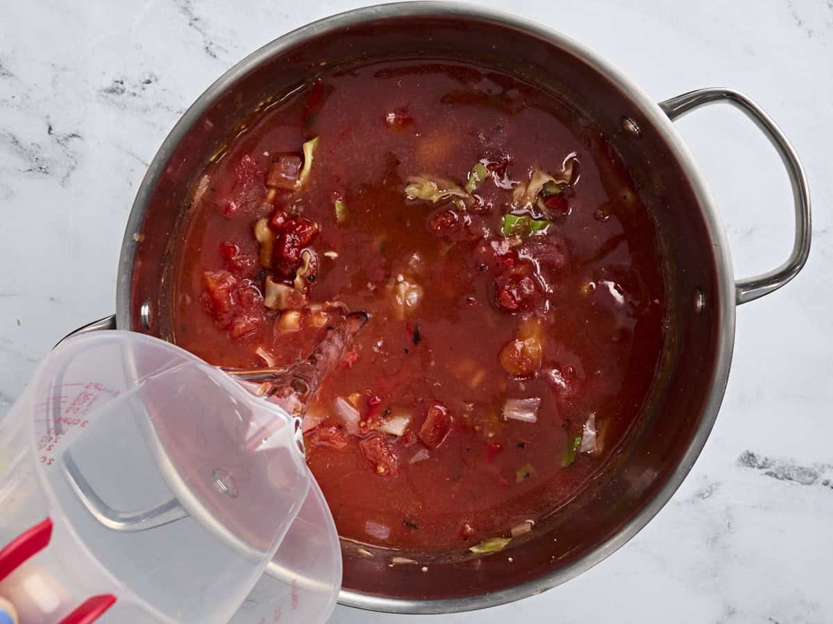 Water being poured into the based for fish soup in a soup pot.