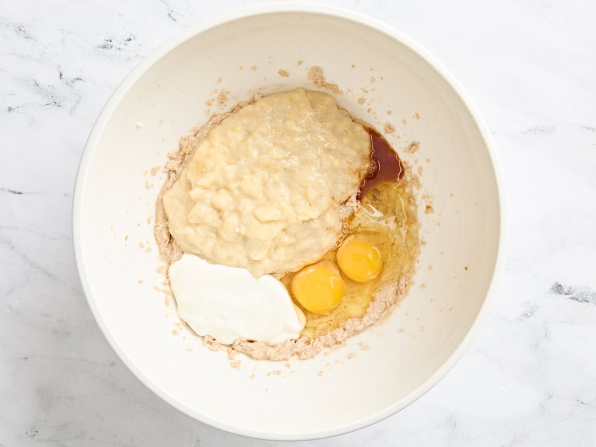 Mashed bananas, yogurt, eggs and creamed butter and sugar in a bowl.
