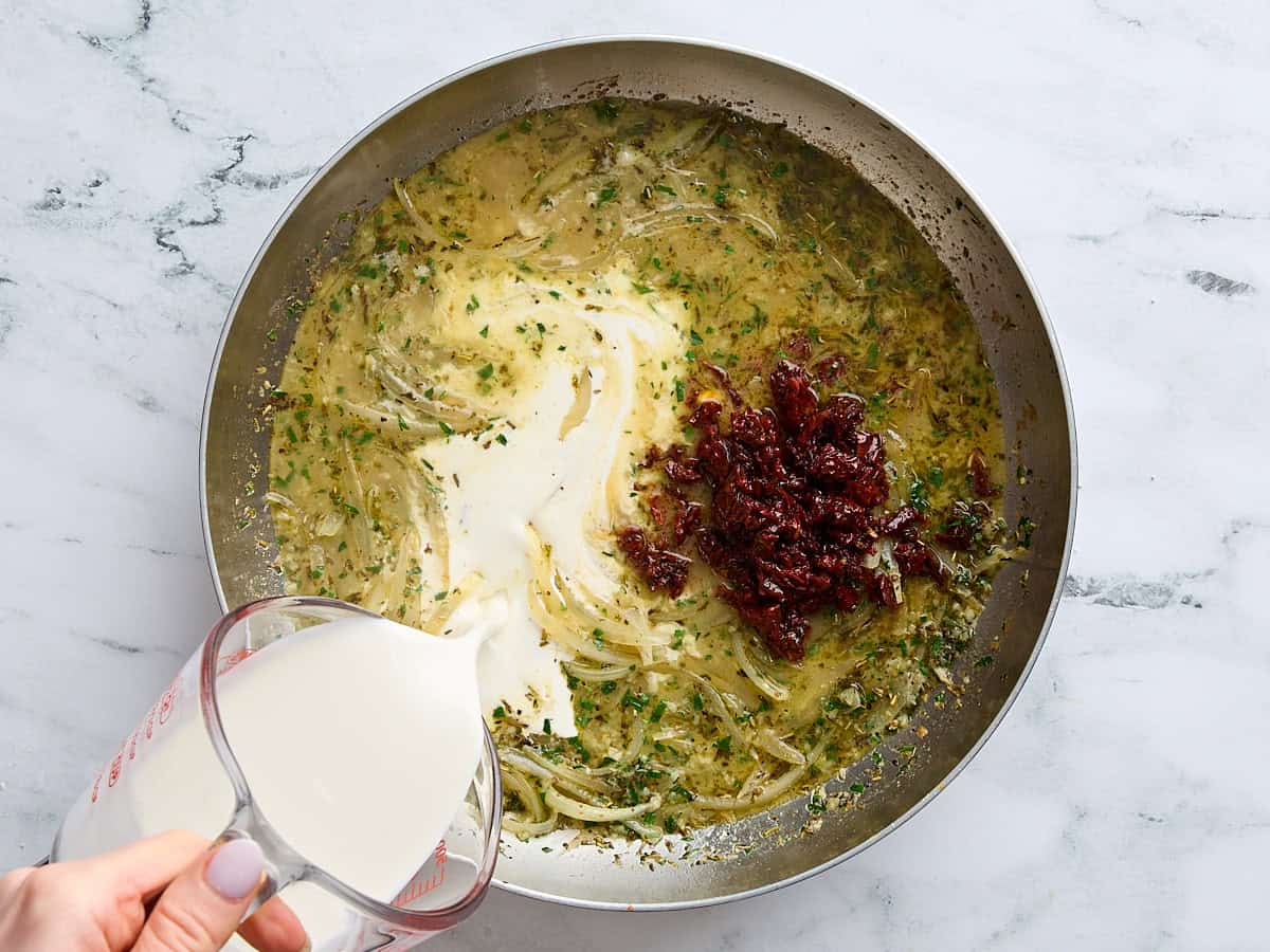 Sundried tomatoes and heavy cream being added to a skillet of onions and broth.