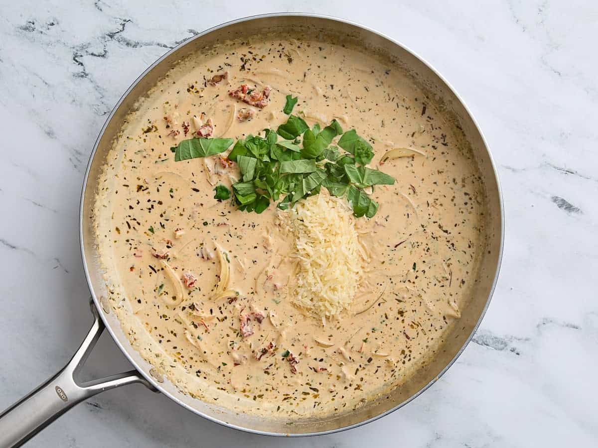 Parmesan cheese and fresh basil added to the sauce for marry me chicken in a skillet.