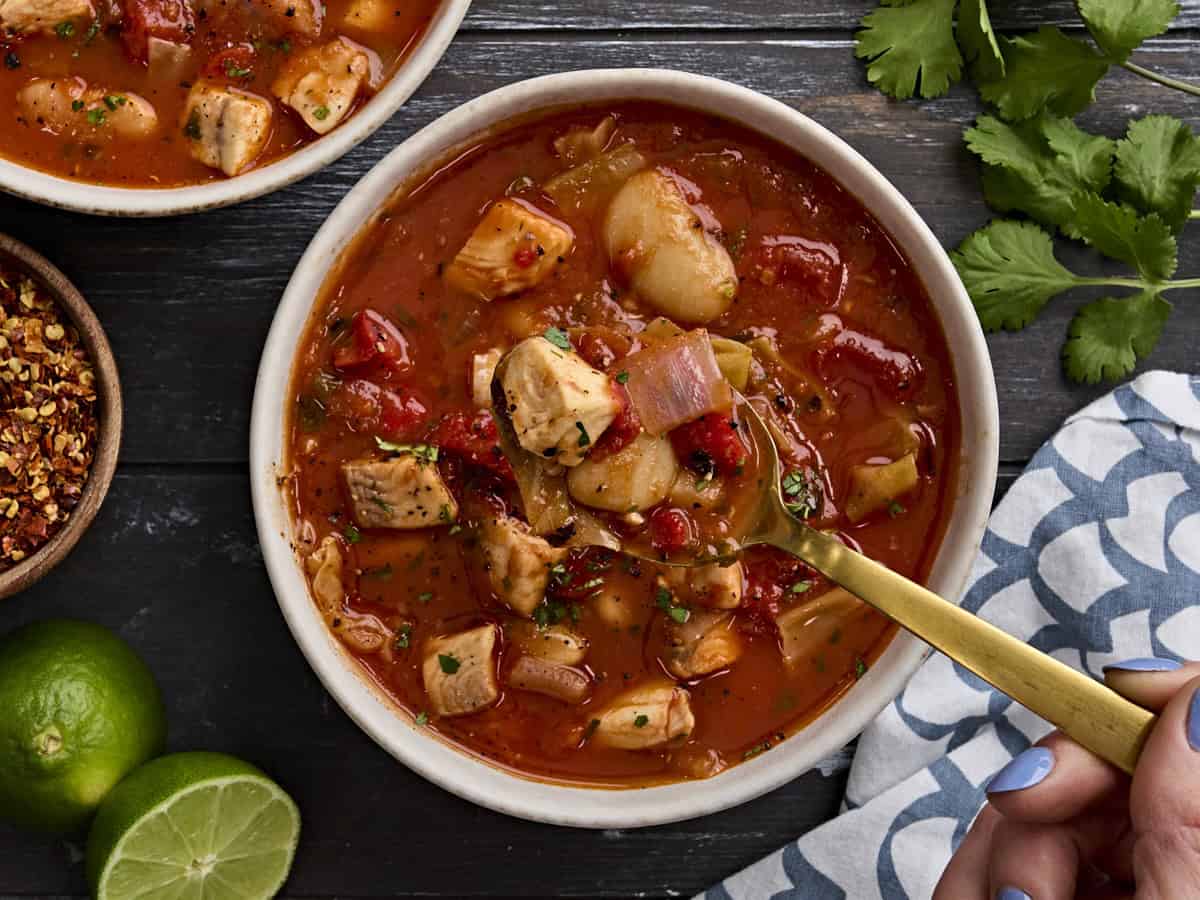 Overhead view of a bowl of fish soup, with a spoon taking some.