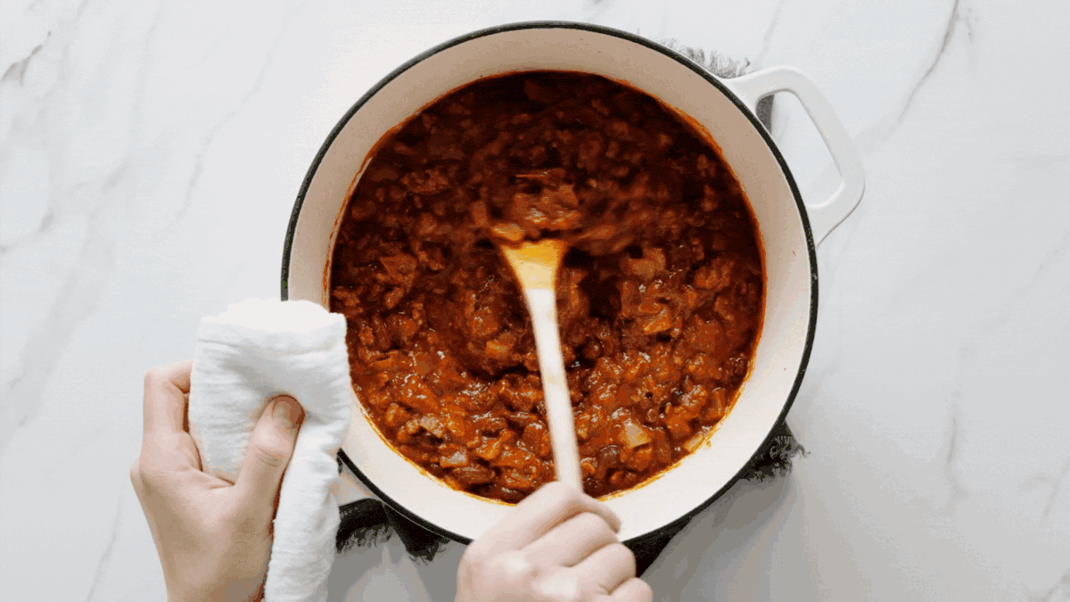 A pot of Chili with Toppings and a wooden spoon