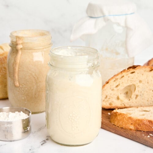 Side view of two jars of sourdough starter with a loaf of sourdough bread.