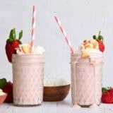 Side view of two strawberry cheesecake smoothies, topped with whipped cream, crumbled cookies, and strawberries.