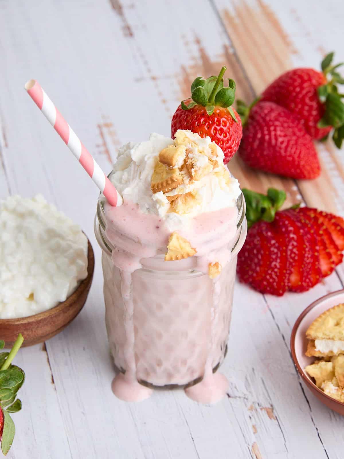 A glass of strawberry cheesecake smoothie, topped with whipped cream and crumbled cookies.