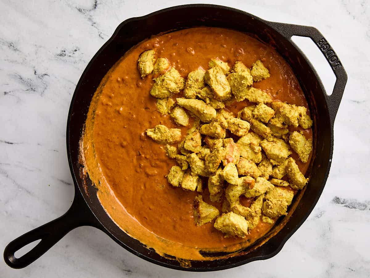Marinated and cooked diced chicken breast added to butter chicken sauce in a skillet.