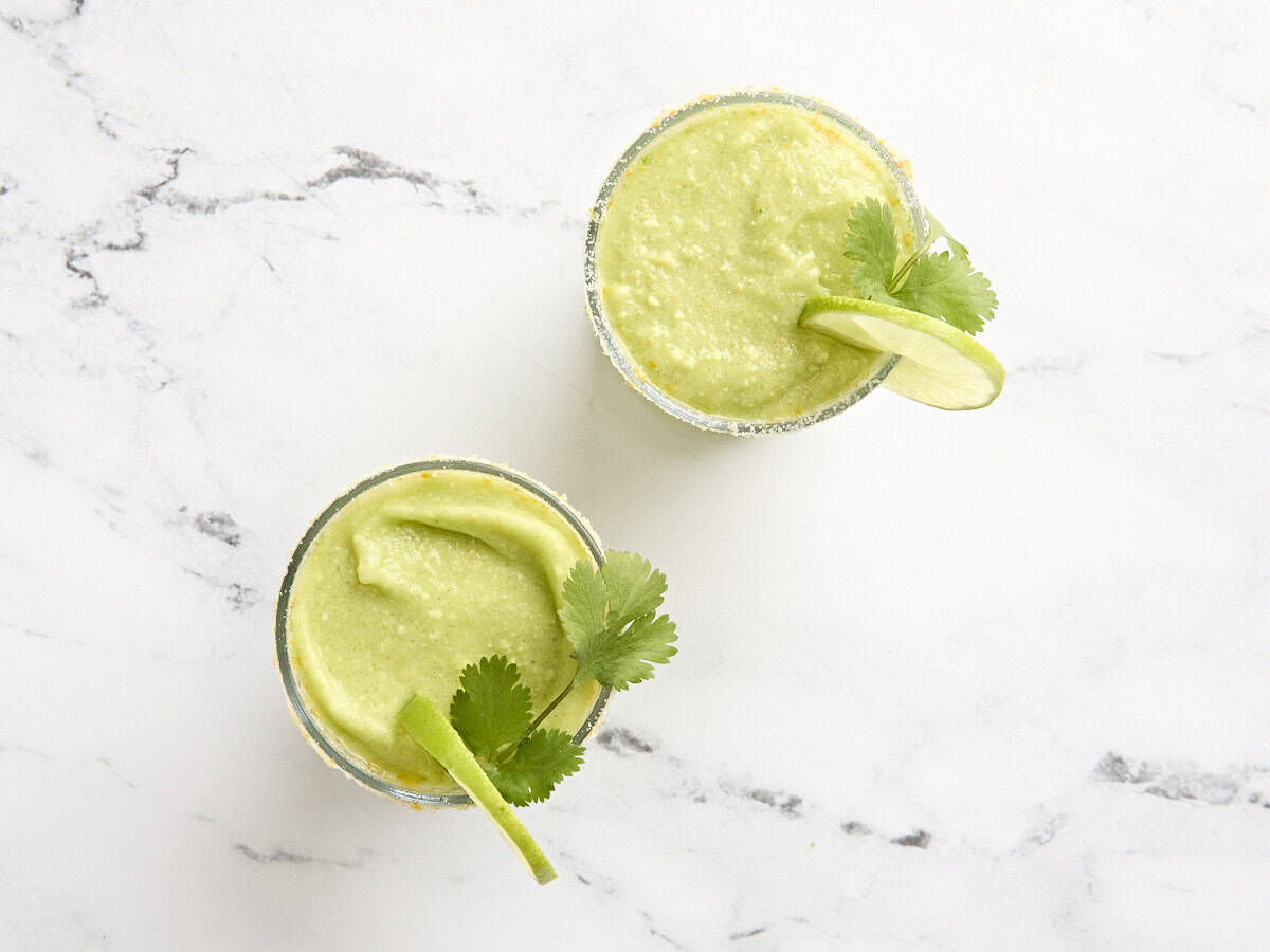 Two glasses of avocado margarita, garnished with lime slices and fresh cilantro.