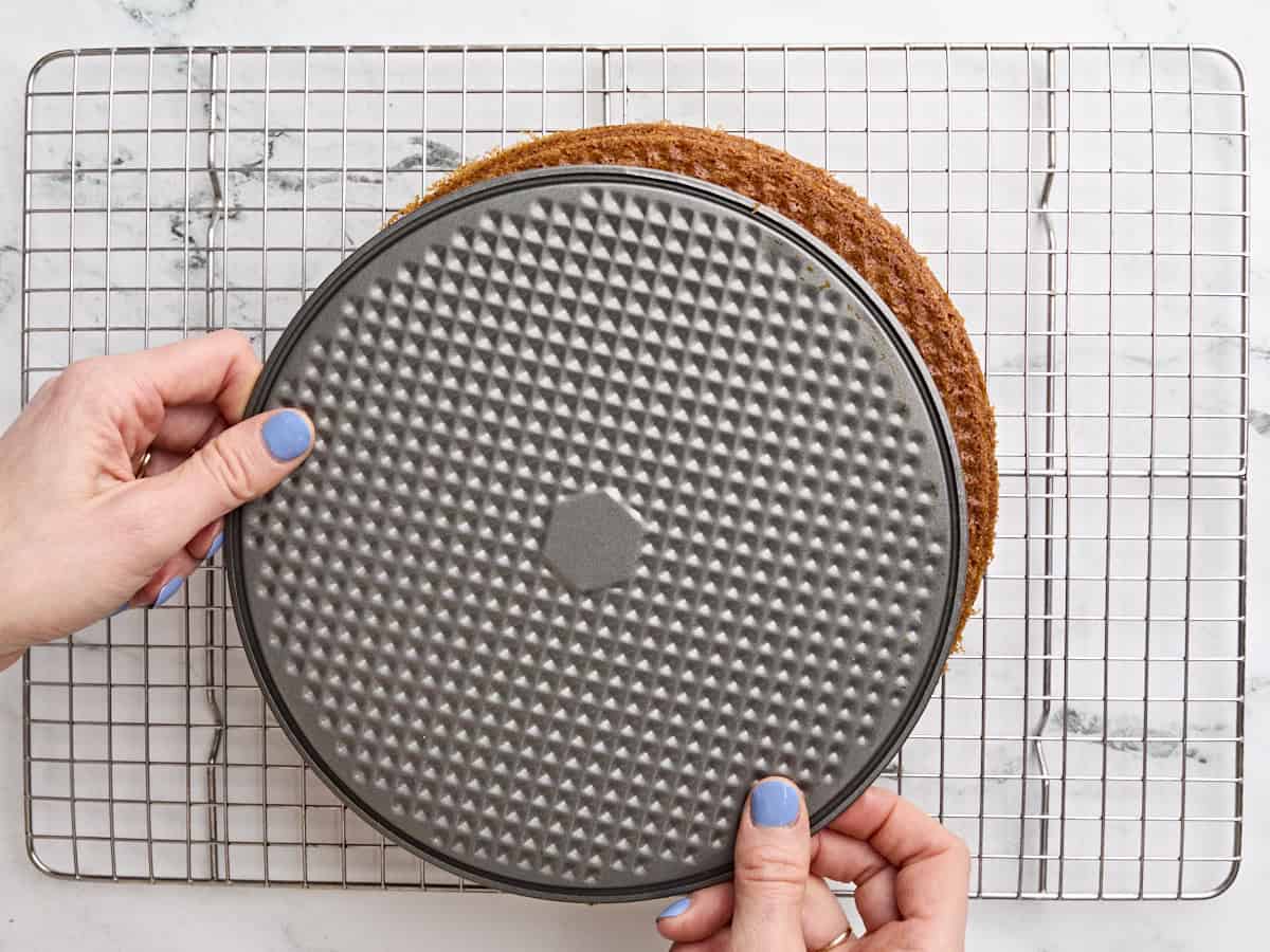 Hands flipping a homemade corn bread cake from the cake pan onto a wire rack.