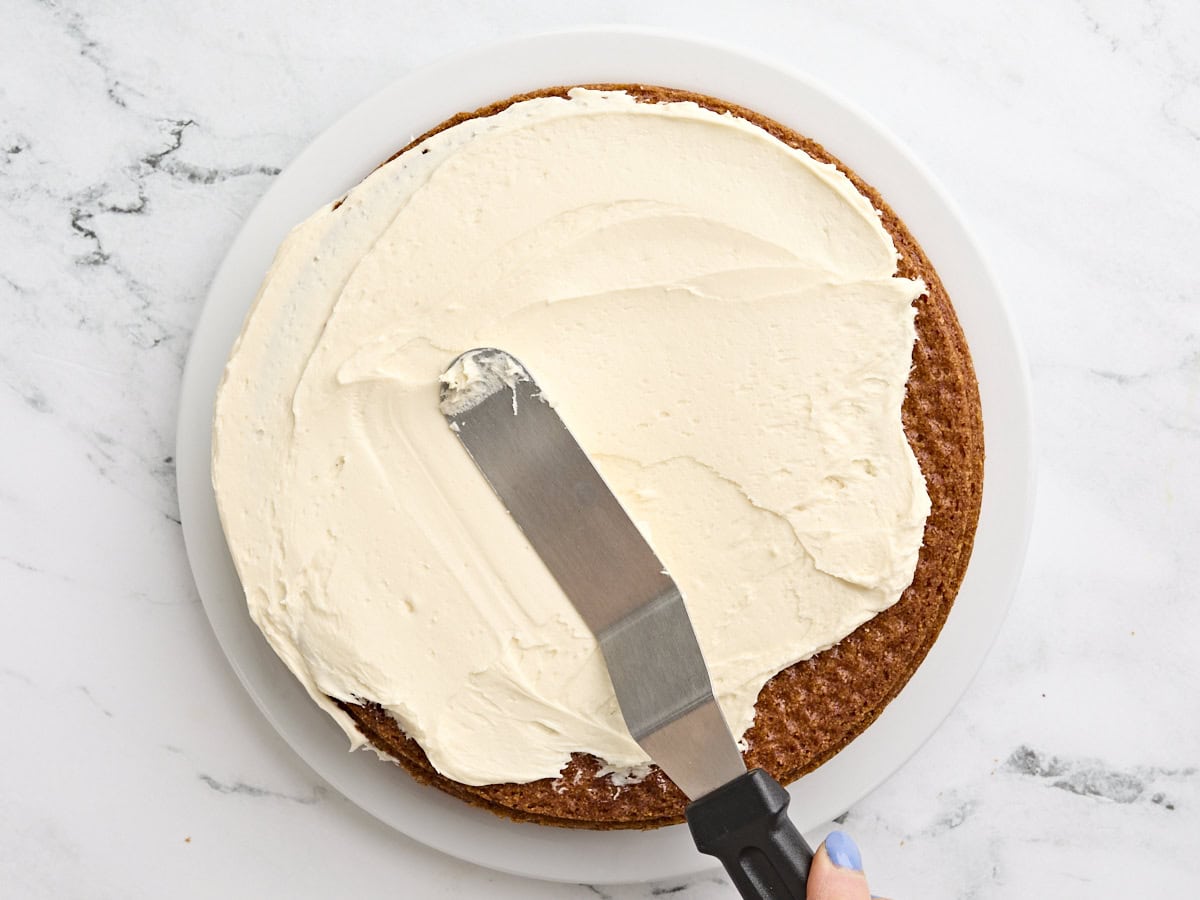 A spatula spreading honey butter cream over a cooled cornbread cake.