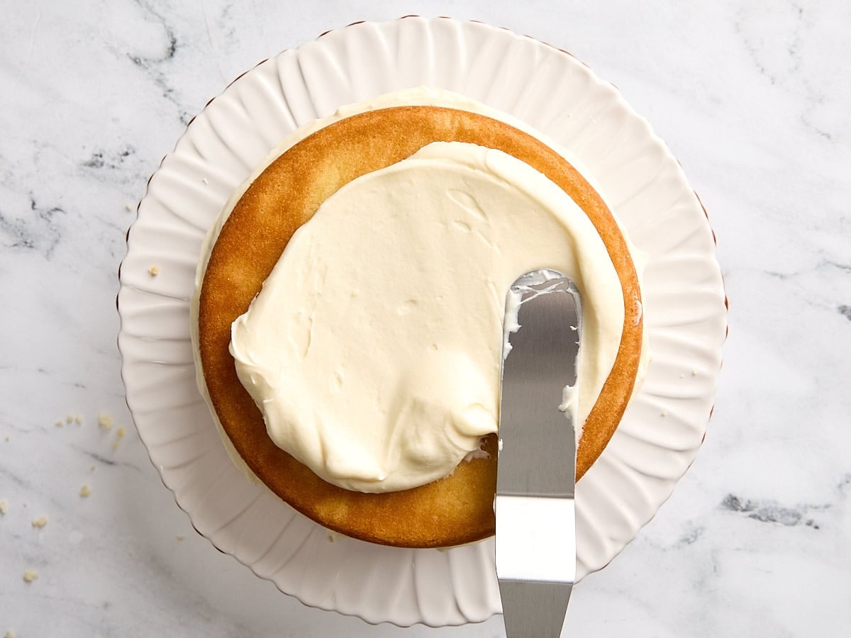 A spatula spreading coconut cake frosting on top of a cake.