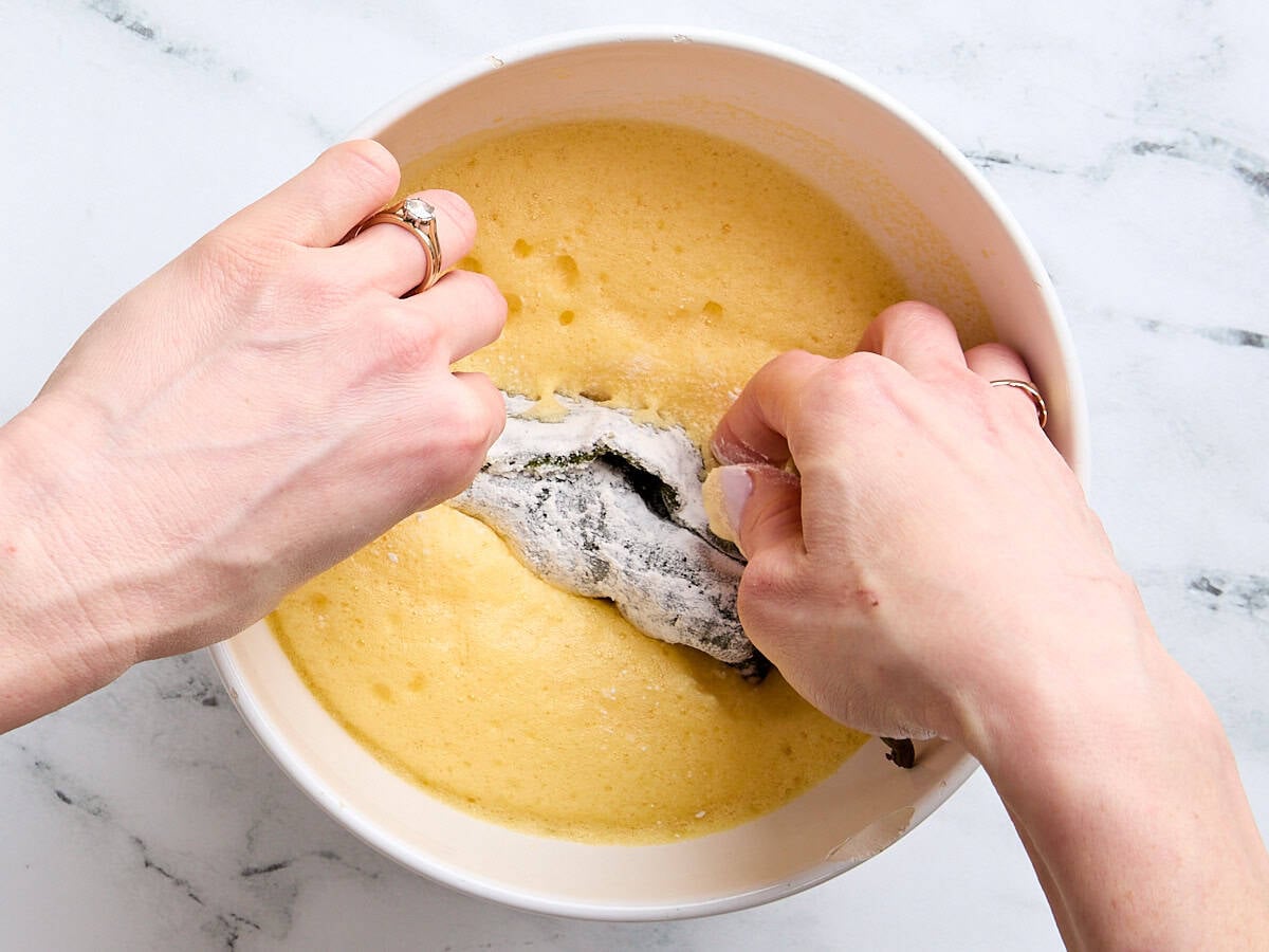 A flour-dipped roasted poblano pepper being dipped into a whipped egg batter.
