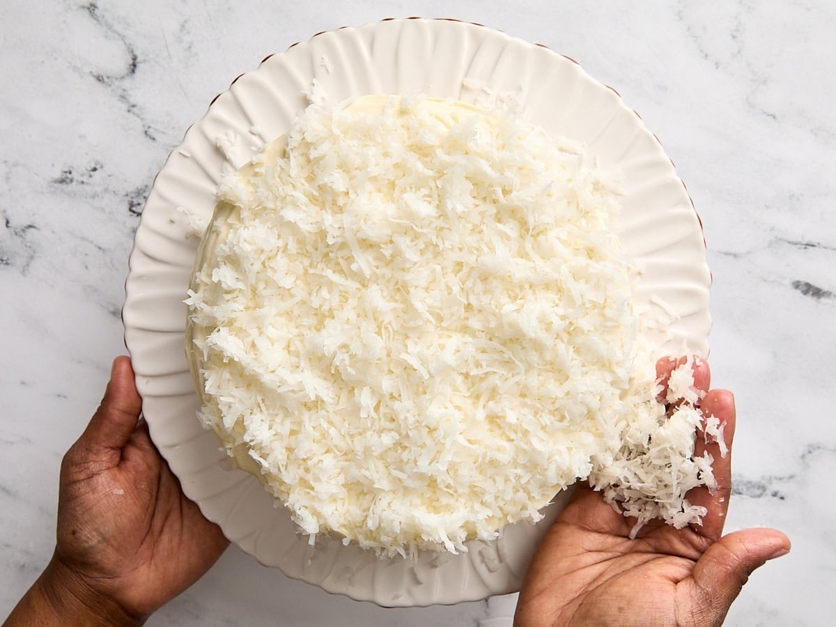 Shredded coconut being added to the frosting of a cake.