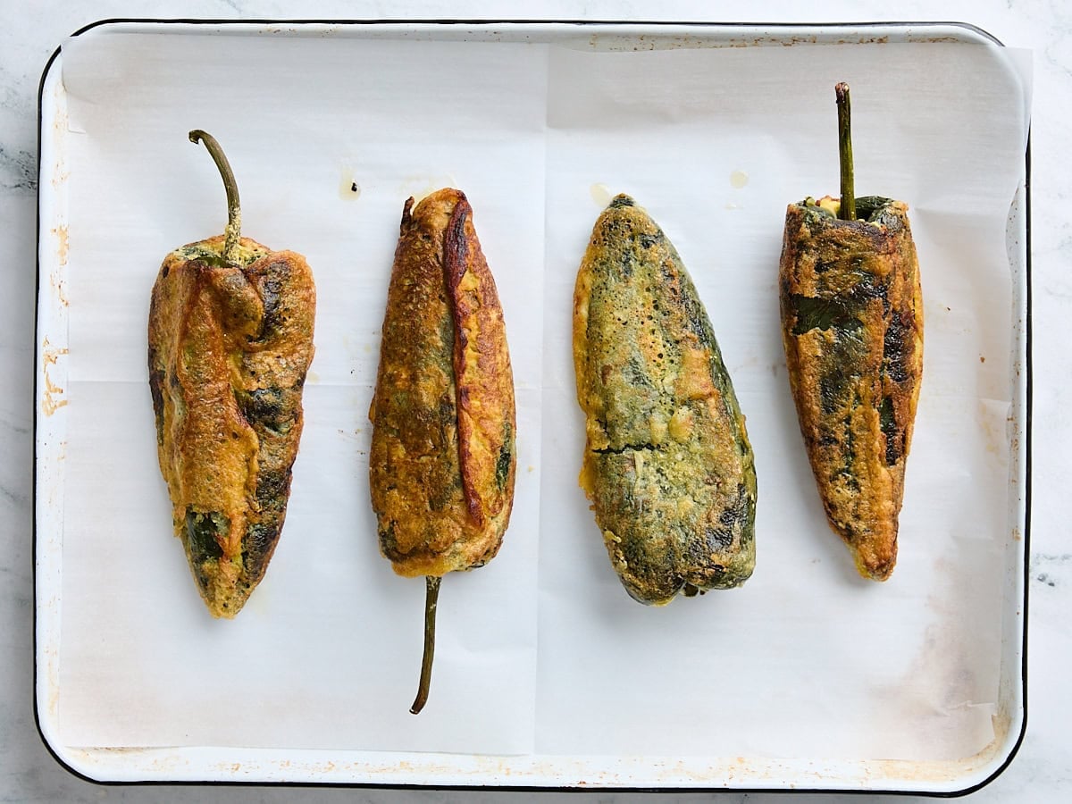 Finished homemade chile rellenos on a parchment lined baking sheet.