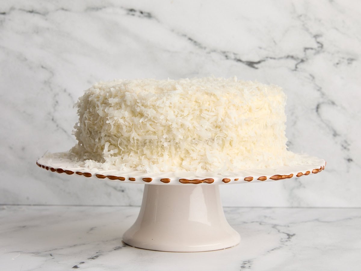 A homemade coconut cake on a cake stand.