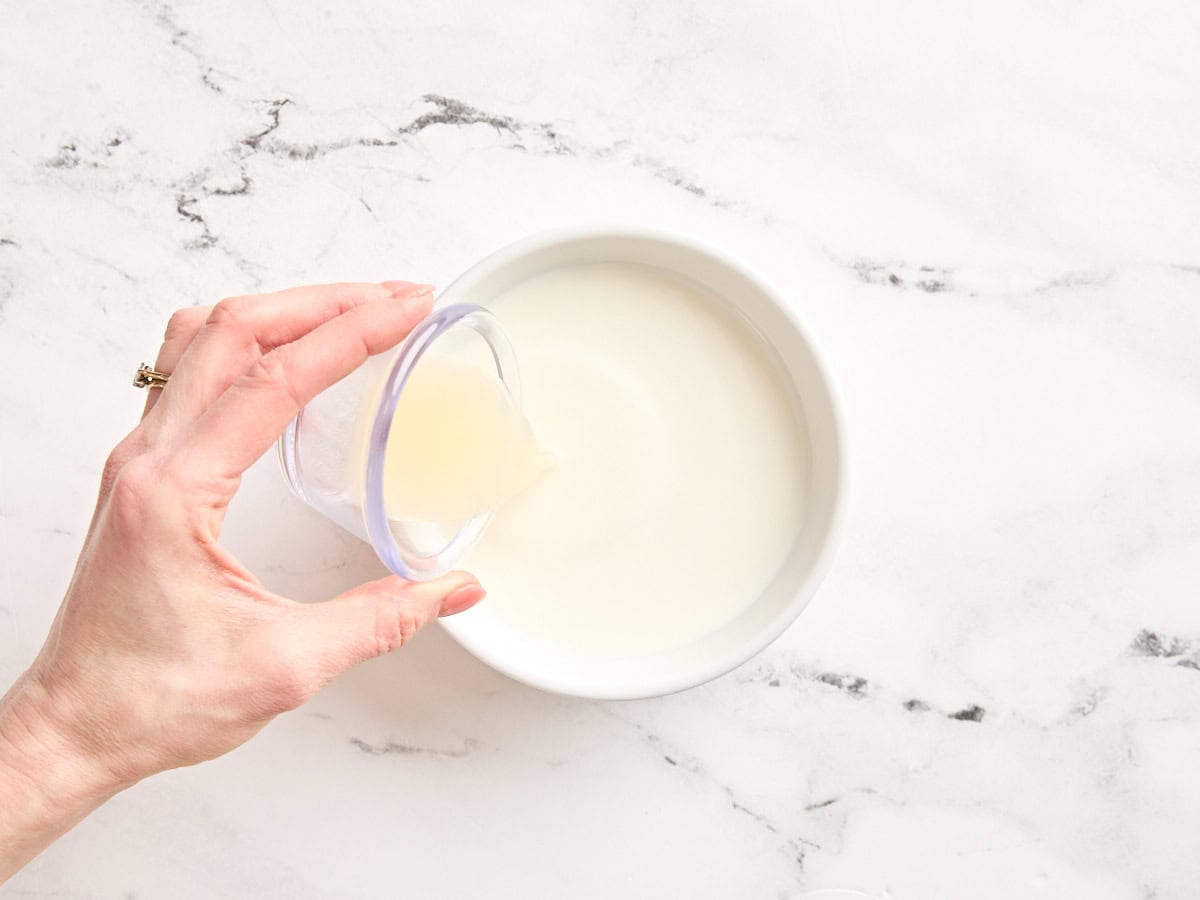 Lemon juice being poured into a bowl of whole milk.