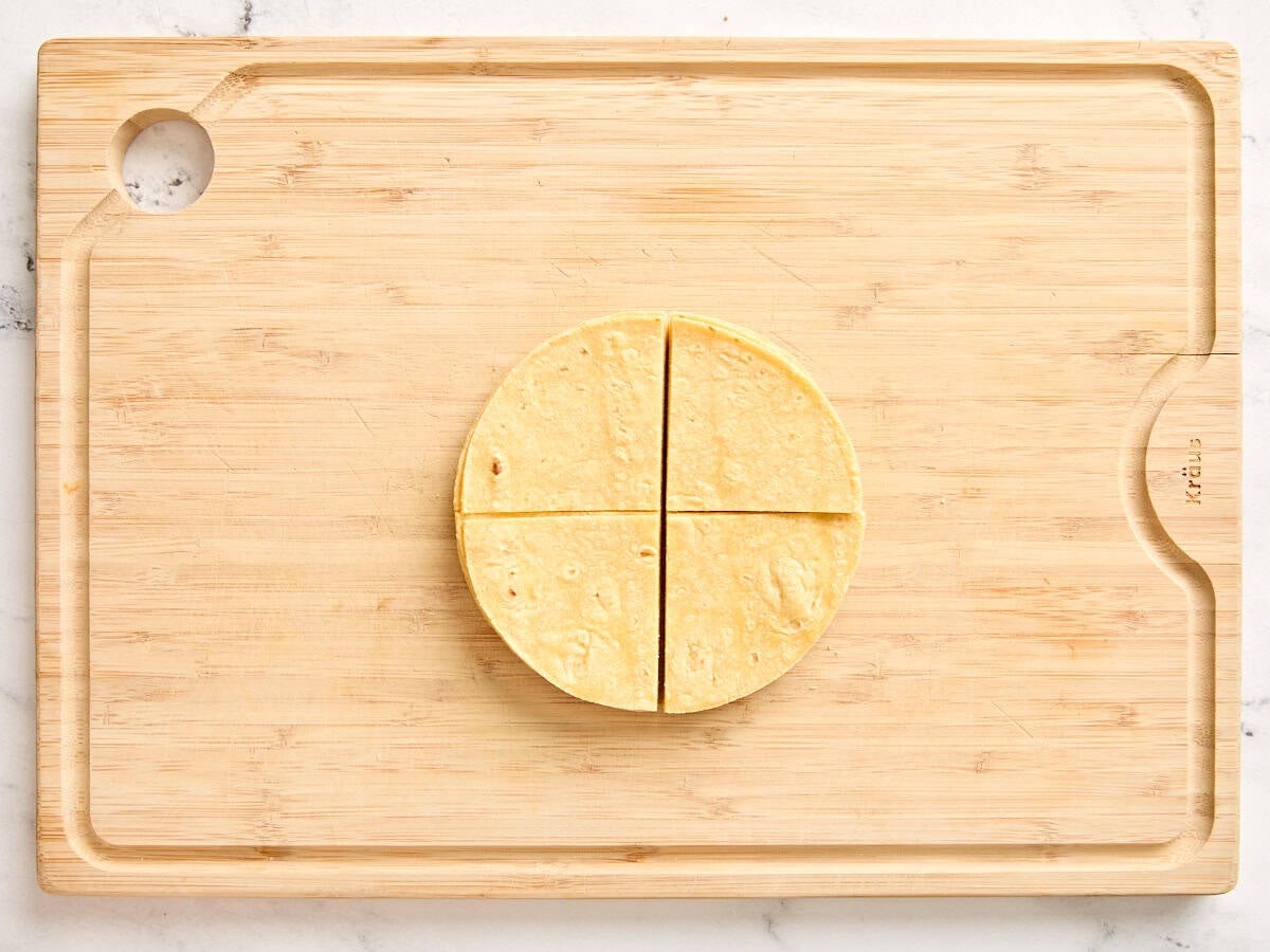 A corn tortilla on a wooden cutting board, cut into quarters.