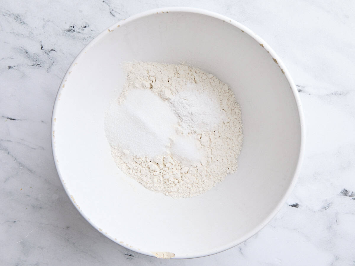 Flour, baking powder, sugar. and salt in a white mixing bowl.