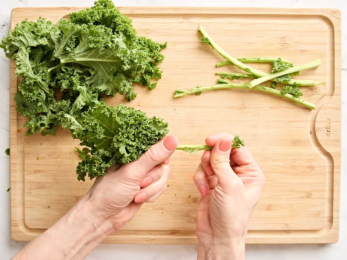 Hands removing the stems from a bunch of kale.