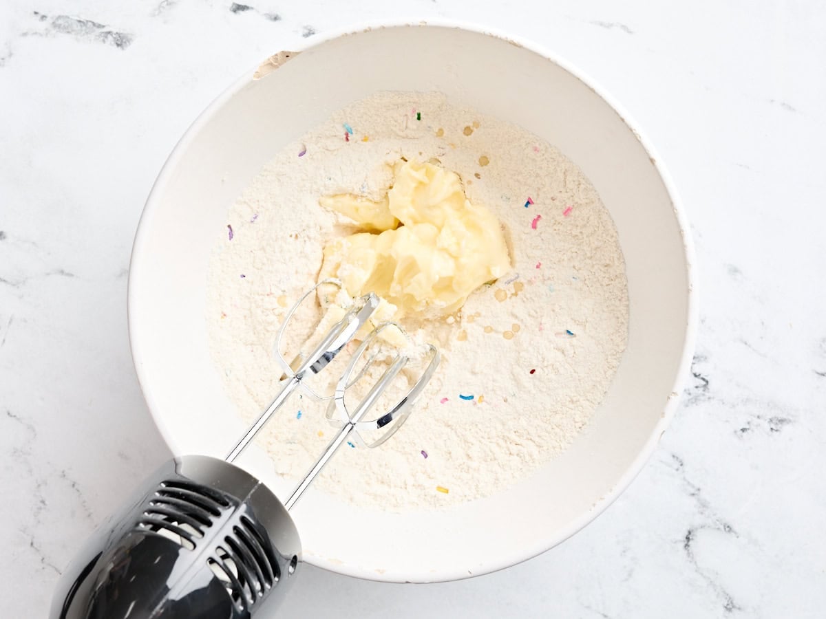 Butter added to the bowl of dry ingredients for sugar cookie bars.