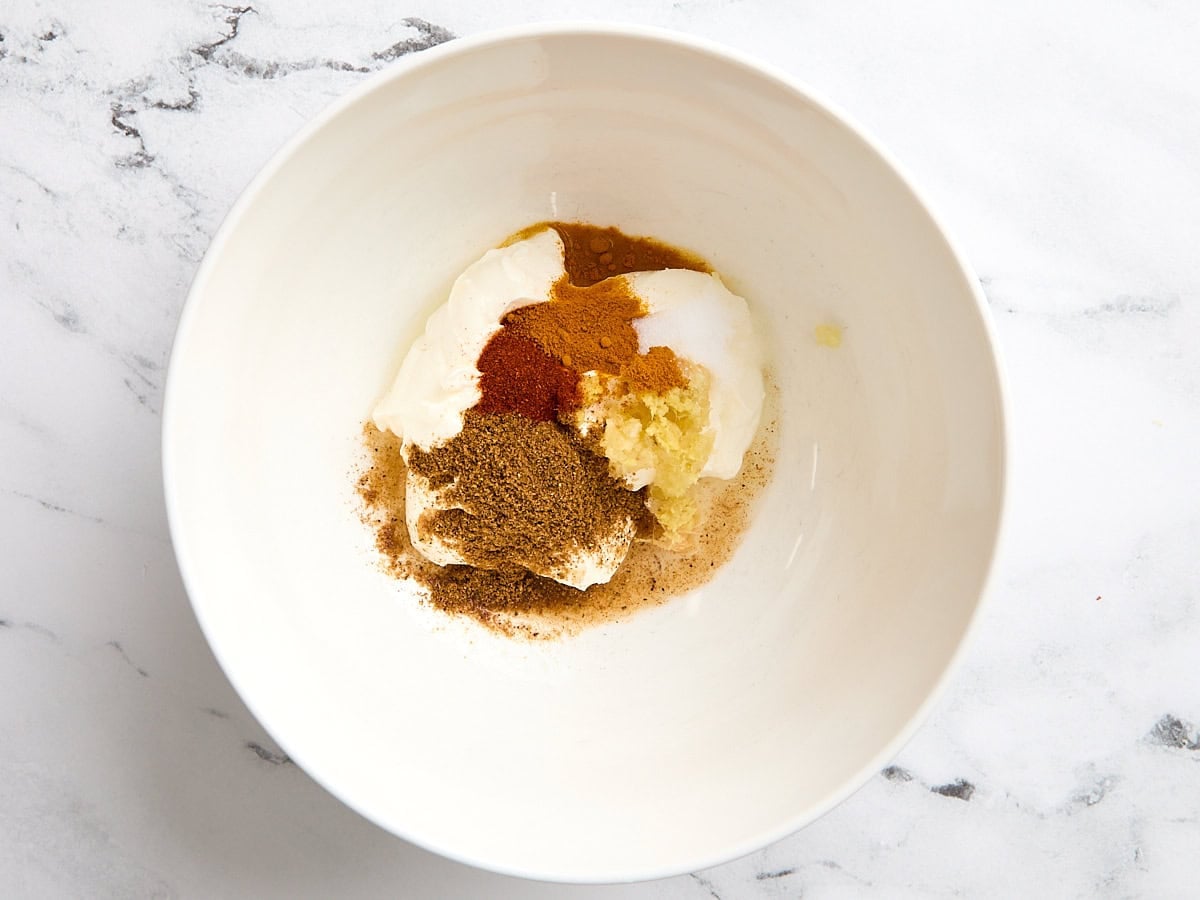 Greek yogurt and spices in a mixing bowl to make a marinade for butter chicken.