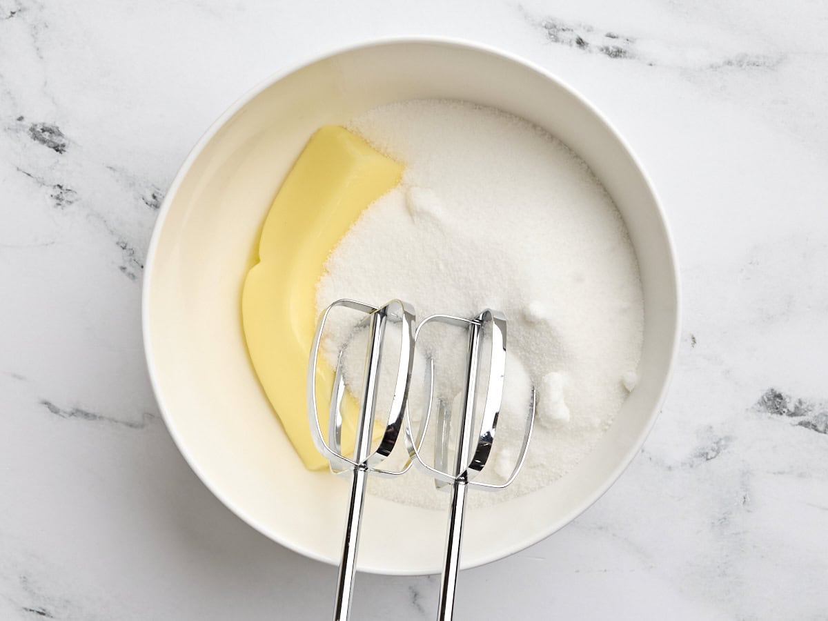 A hand mixer about to cream together butter and sugar in a bowl.