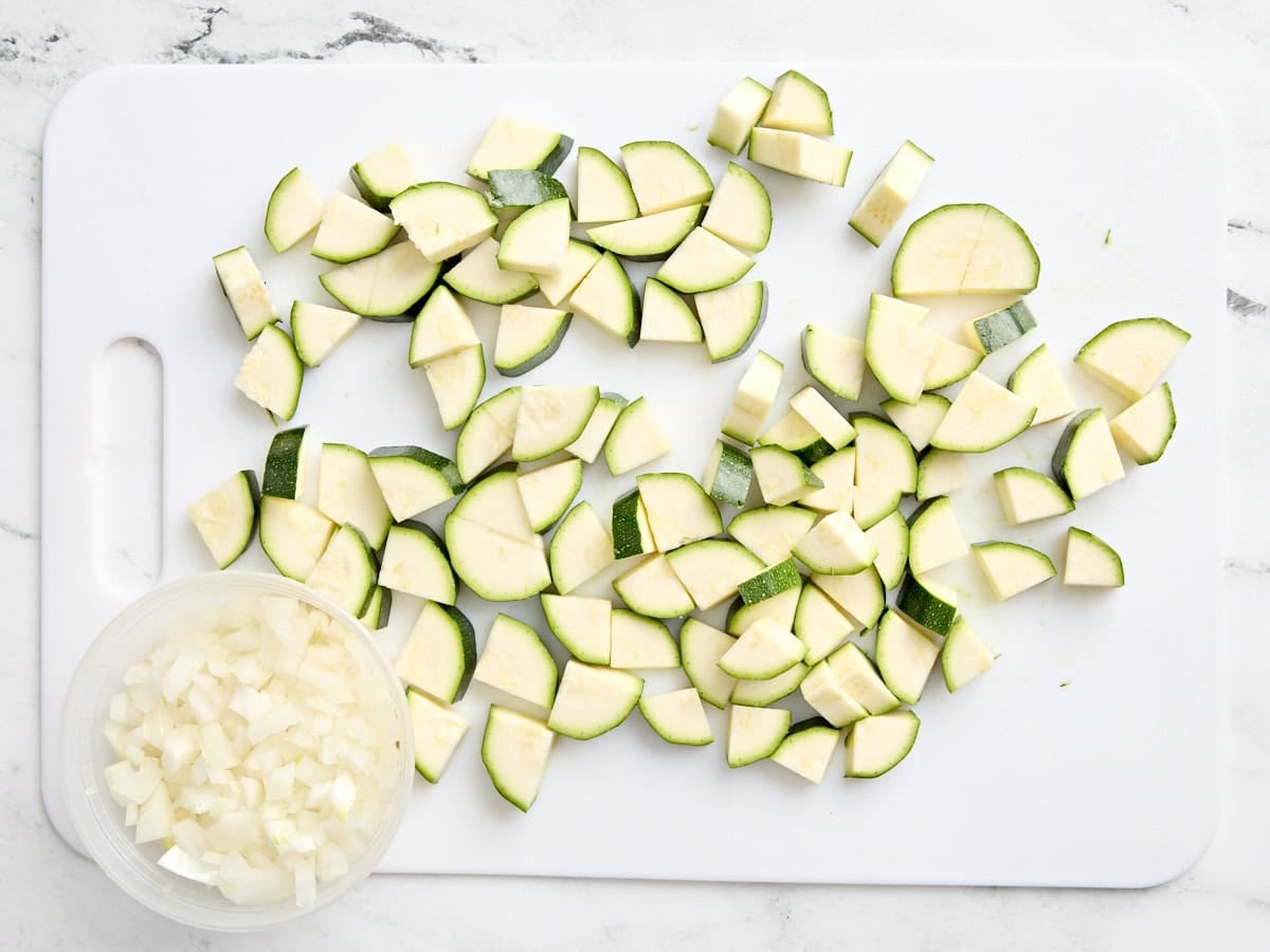Diced onion and quartered zucchini on a white cutting board.