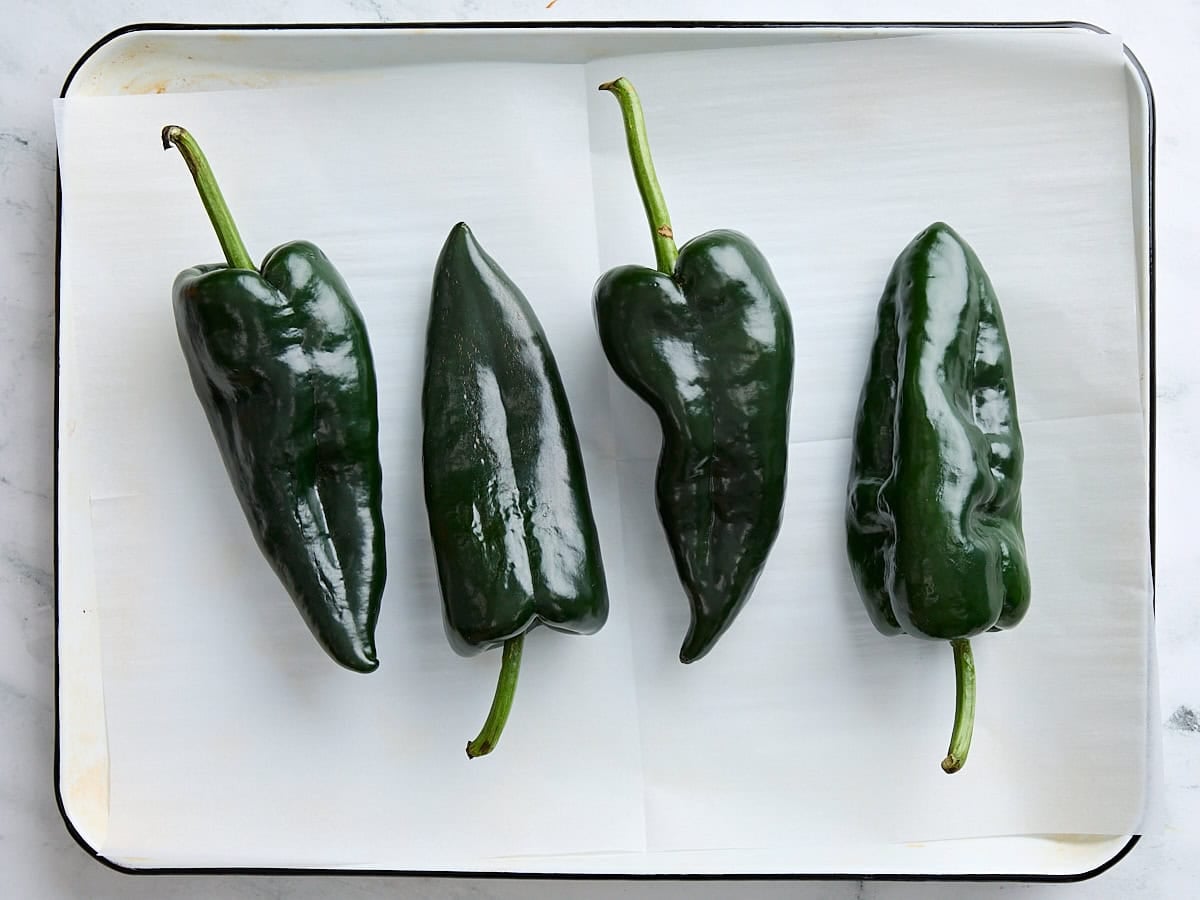 Four poblano peppers on a parchment lined baking sheet.