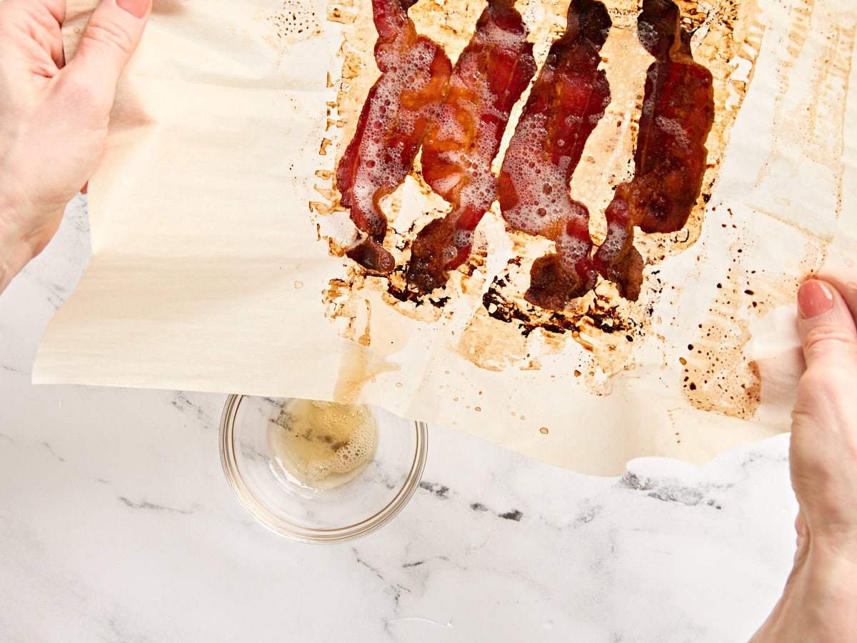 Rendered bacon fat being poured into a glass bowl from cooked bacon.