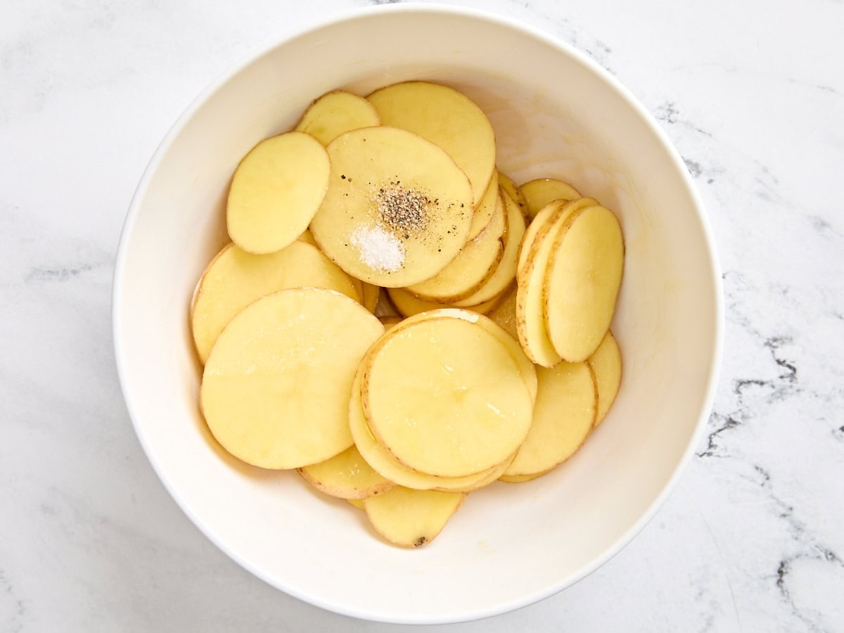 Sliced potatoes in a bowl with seasonings.