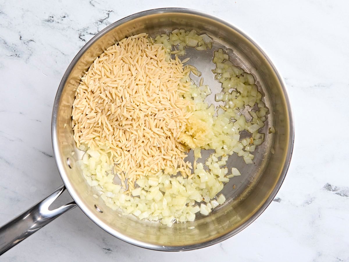 Dried orzo added to a skillet with sauteed onion and minced garlic.