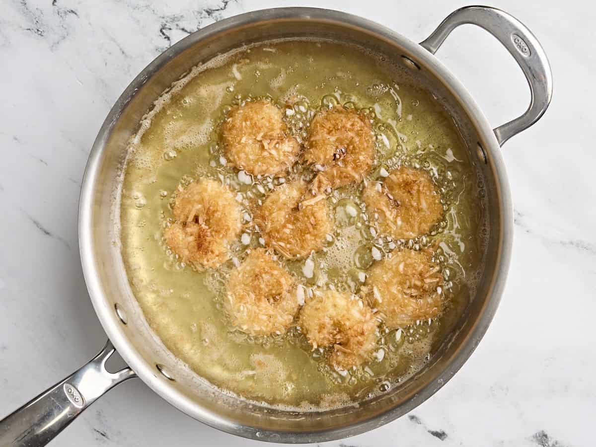 Coconut shrimp frying in a skillet of vegetable oil.