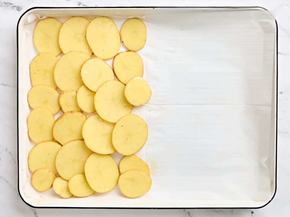 Sliced potatoes laid on 1/3 of a sheet pan.