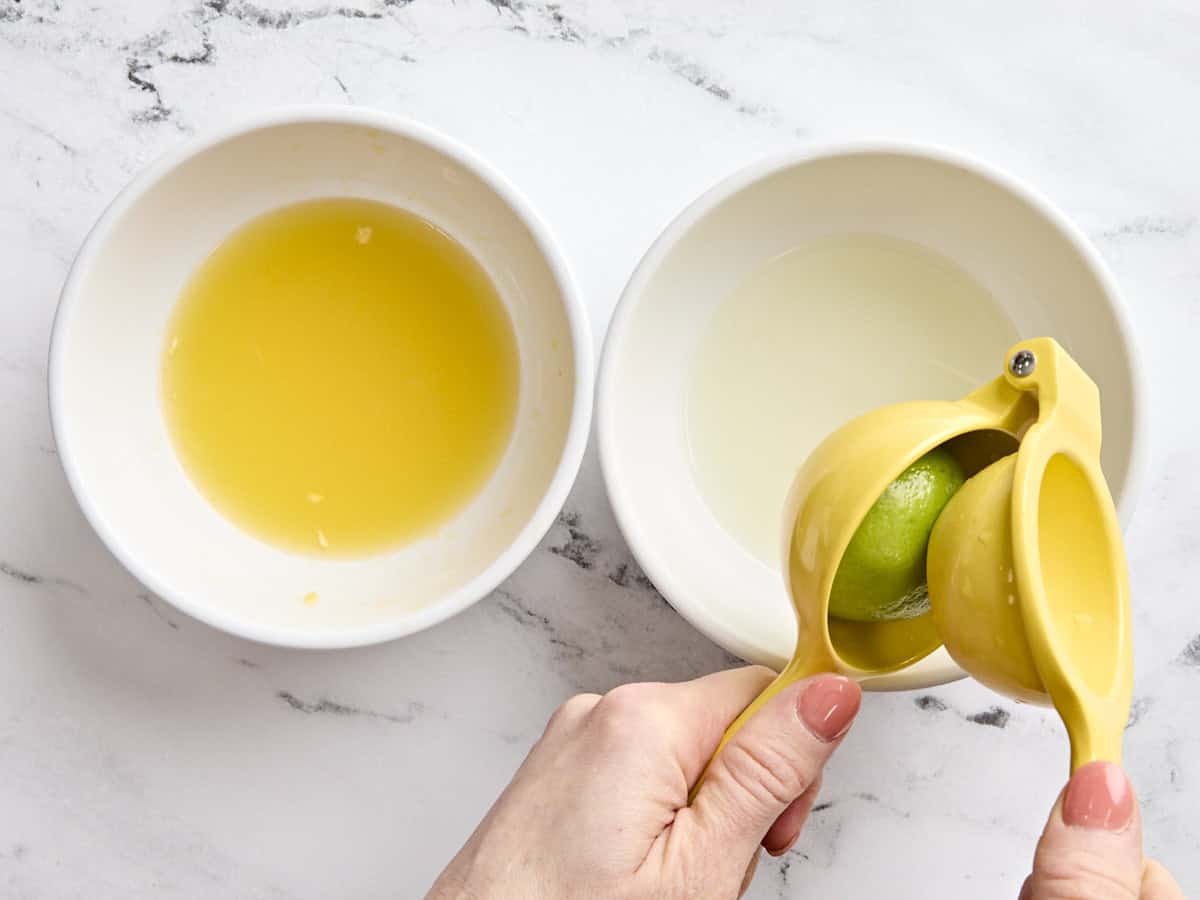 A bowl of orange juice and a hand holding a juicer with a lime in.