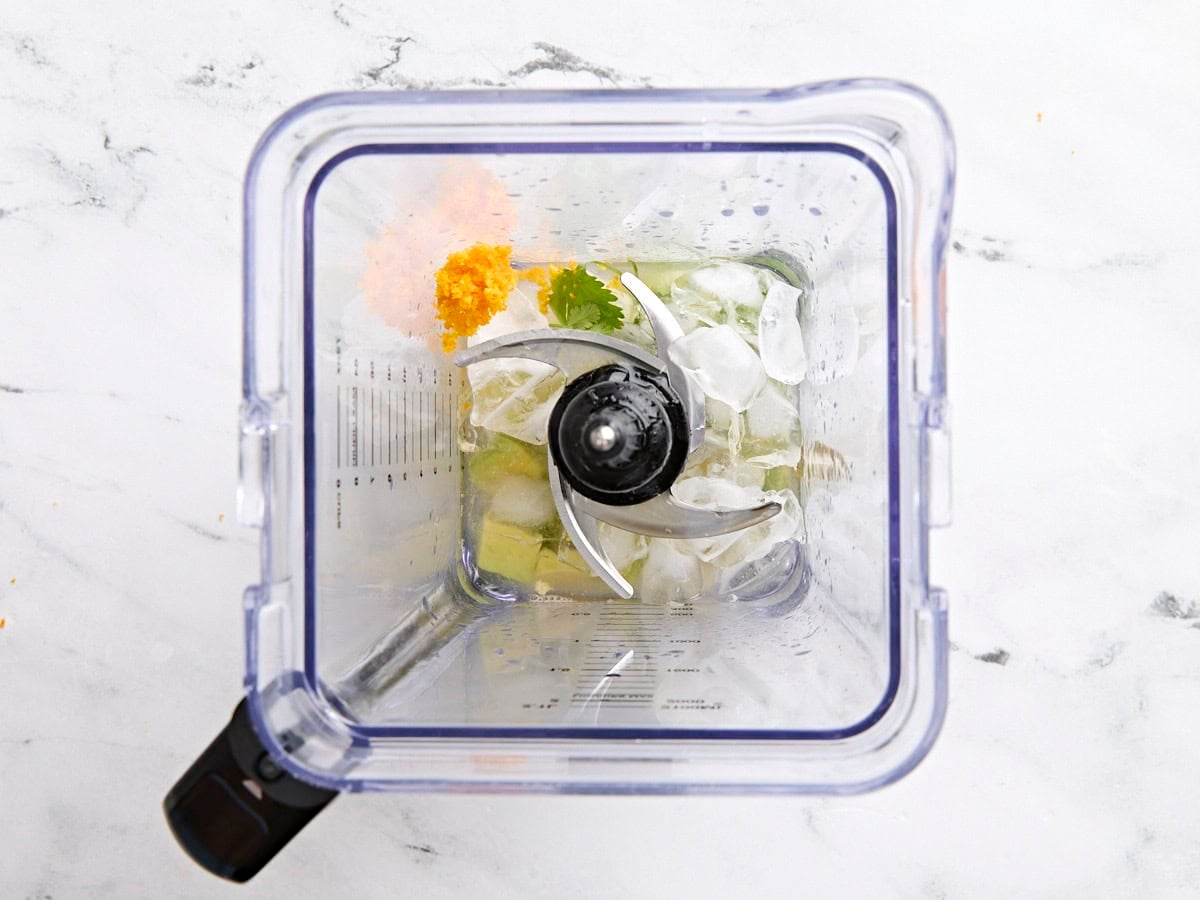 Ice, avocado, cilantro, lime and orange juice in a blender.