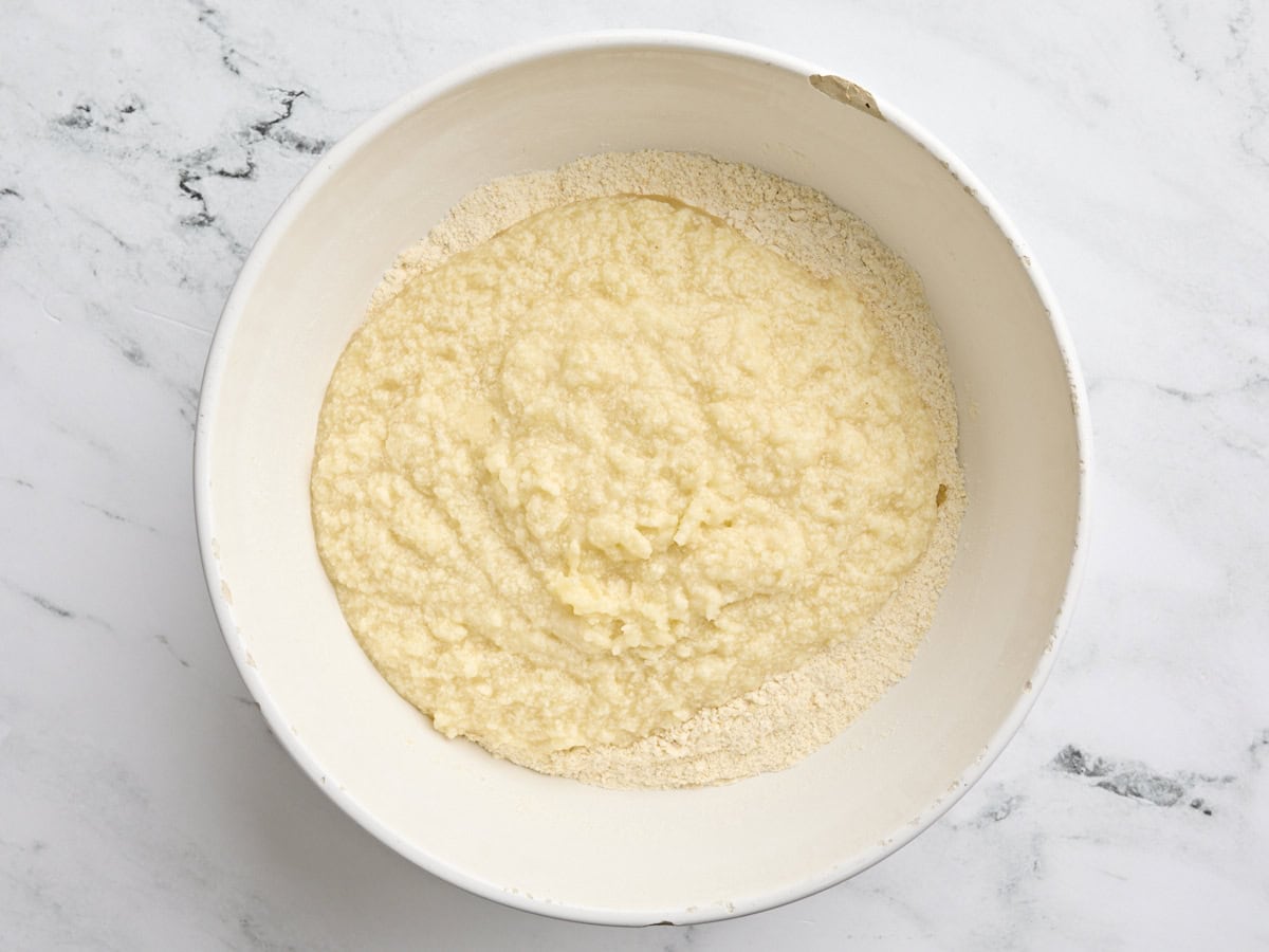 The wet ingredients for cornbread cake added to the dry ingredients in a bowl.