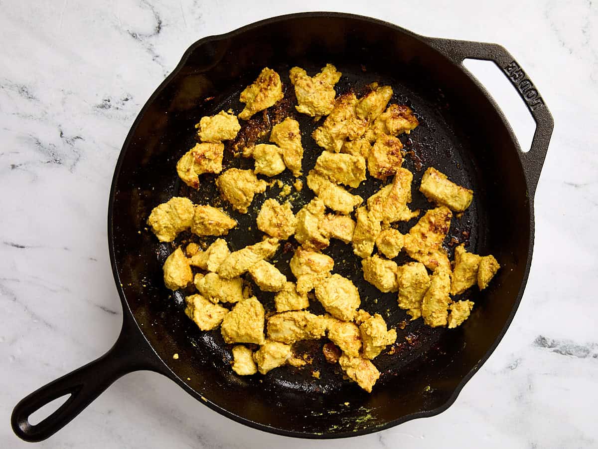 Marinated chicken breast cooking in a cast iron skillet.